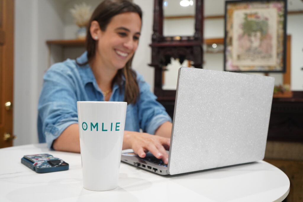 Woman smiling at her computer with an Omlie coffee mug infront of her.