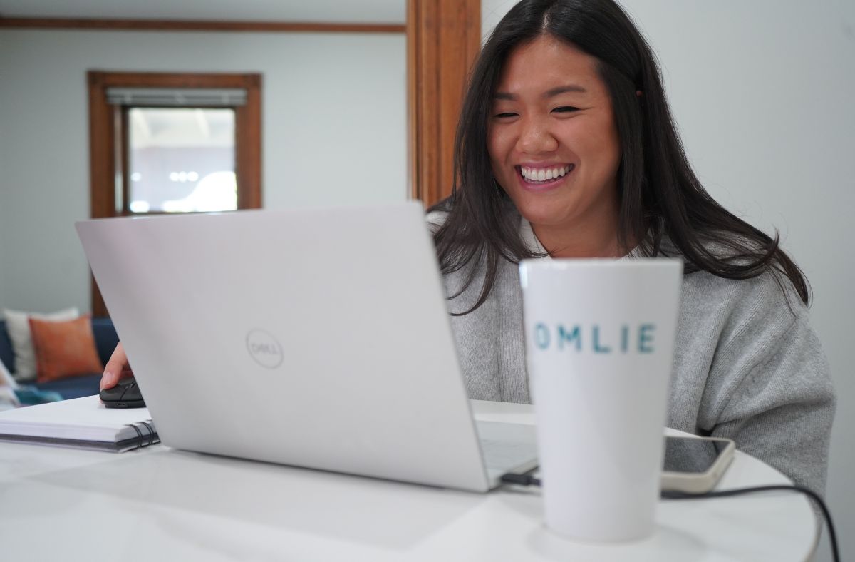 Woman smiling on the computer at the Omlie House with an Omlie mug infront of her.