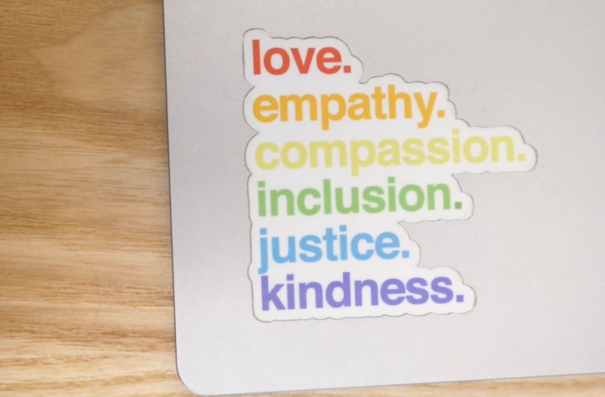 Sticker decal on a computer that reads "Love (red), empathy (orange), compassion (yellow), inclusion (green), justice (blue), kindness (purple)."